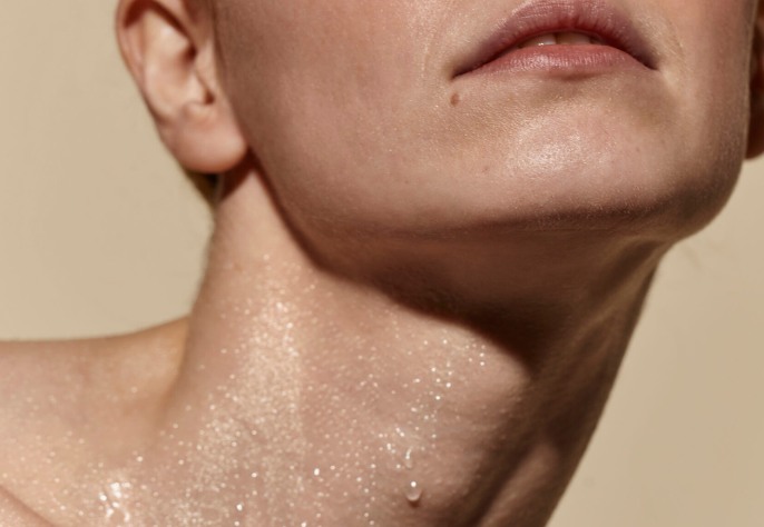 A close-up of a person's neck, jawline, and chin, showing glistening skin with water droplets, conveying deep hydration and a healthy glow.